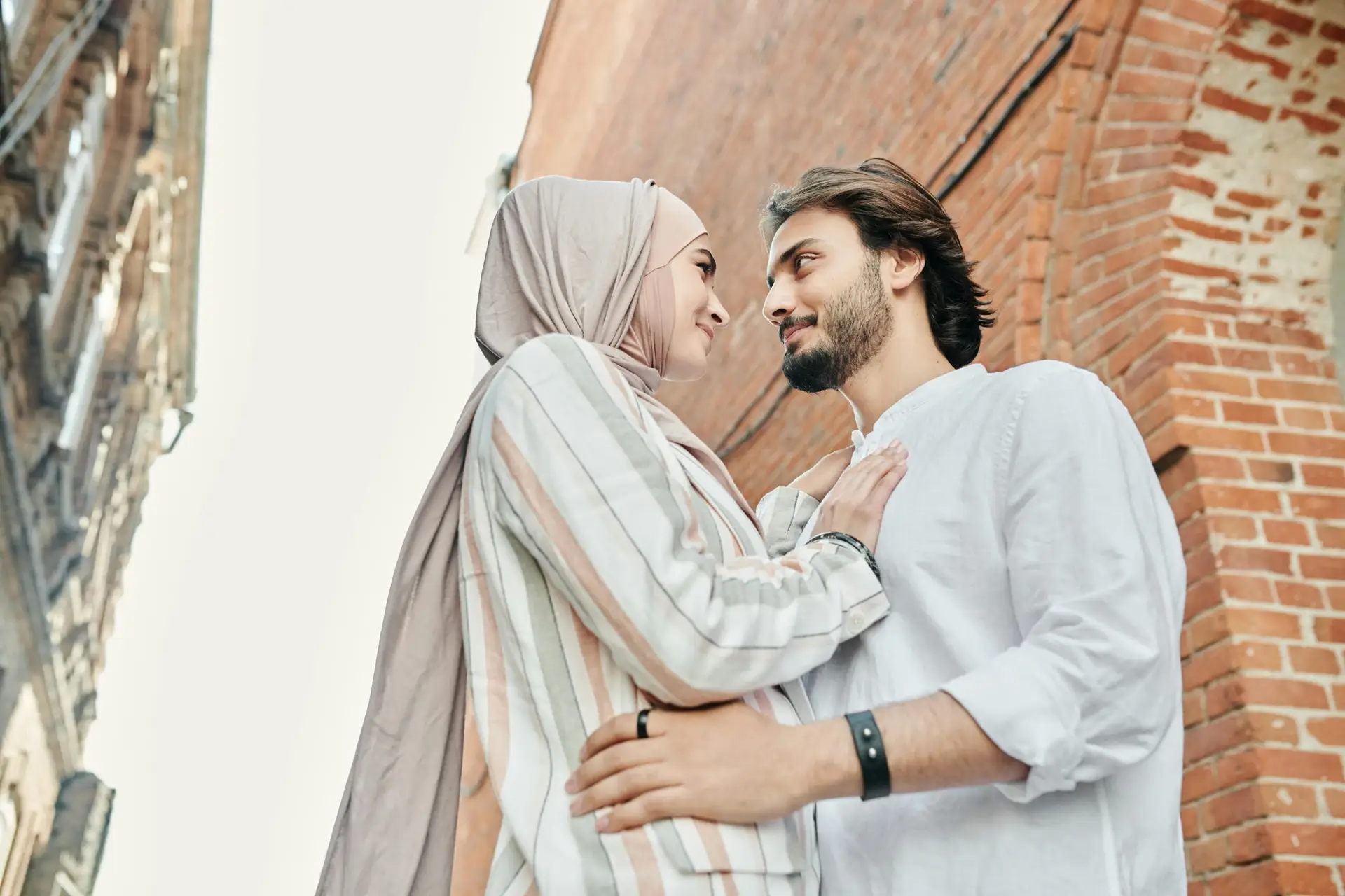 Young couple in love, embracing beside a brick wall, sharing a tender moment outdoors.